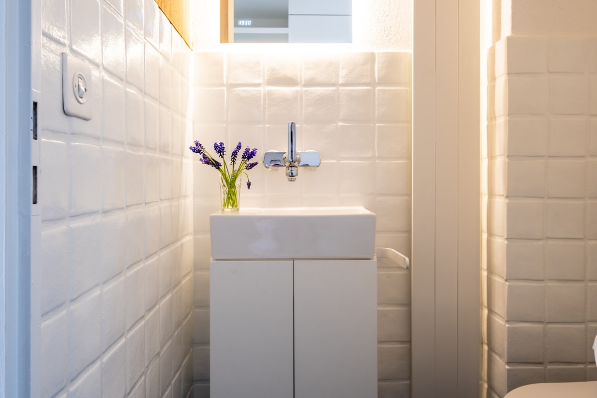 A clean white subway-tiled NYC bathroom with natural light, cleaning spray bottle on the edge of the bathtub
