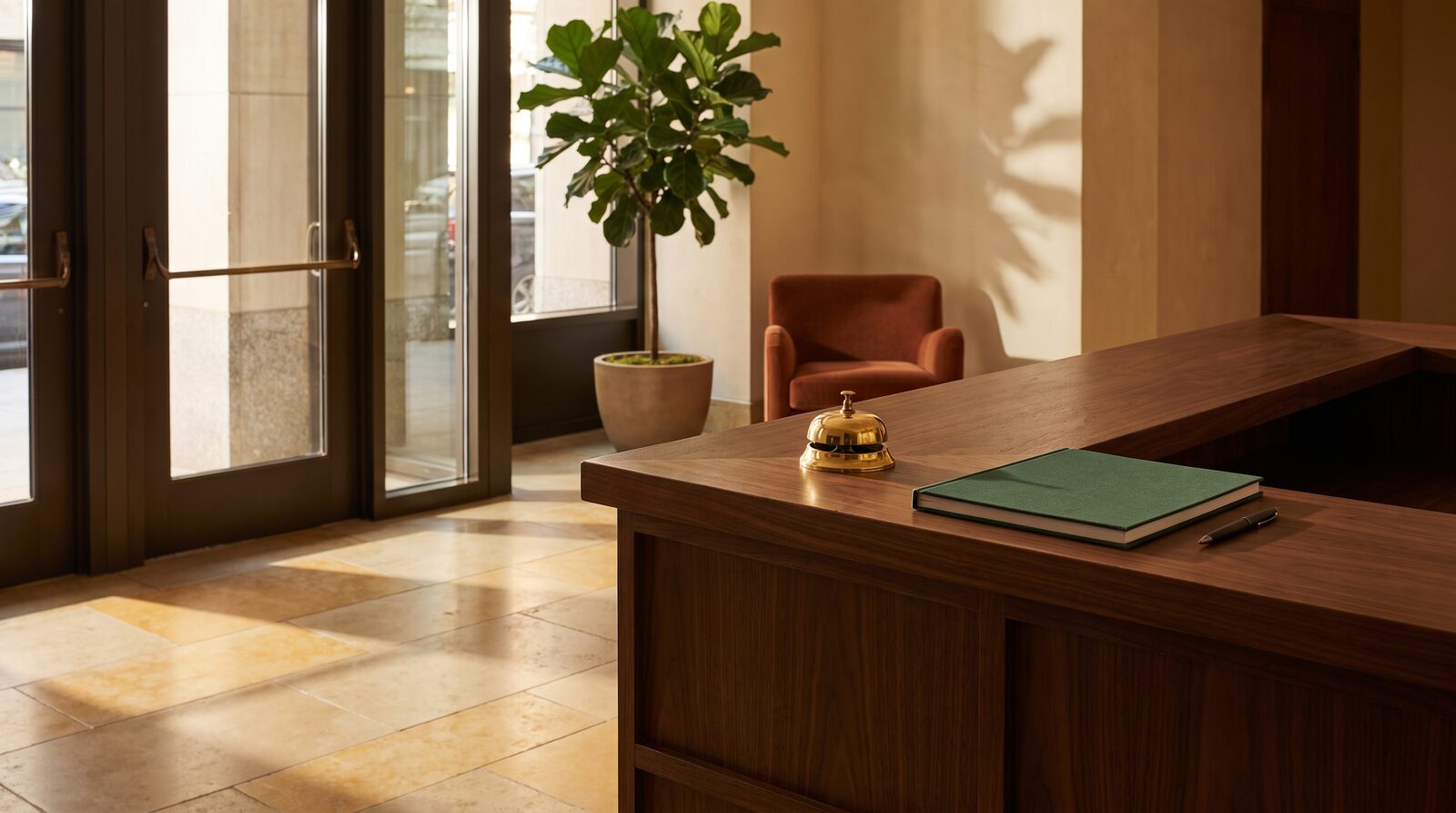 The empty front desk of a NYC doorman building lobby, with a closed guest ledger and a brass call bell on the walnut counter