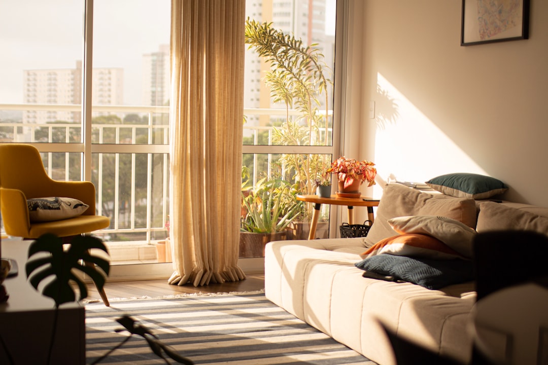 A bright apartment living room with windows cracked open, sheer curtains catching a breeze, clean and calm with no clutter