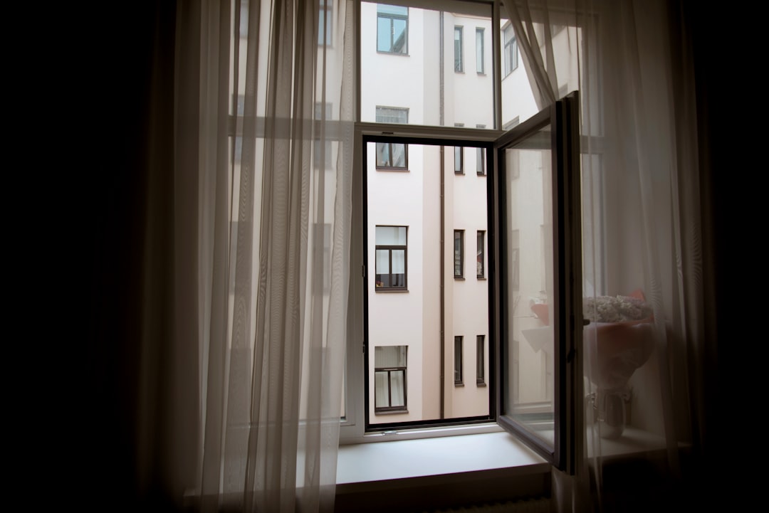 An open window in a NYC apartment with sheer curtains slightly blowing inward, rooftop water towers visible in the background
