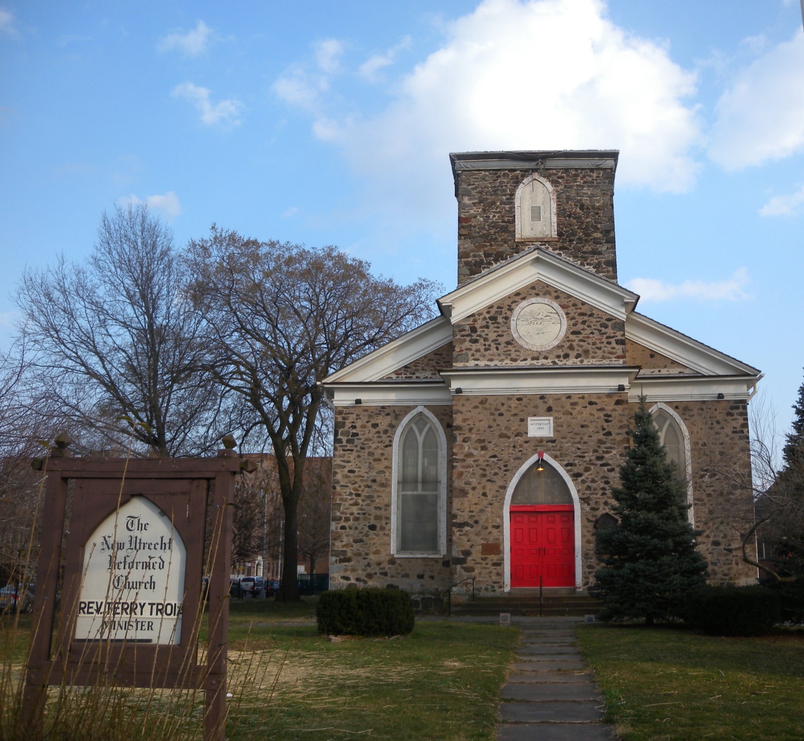The stone Georgian Gothic facade of the New Utrecht Reformed Church at 84th Street and 18th Avenue in Bensonhurst Brooklyn with its red entrance doors