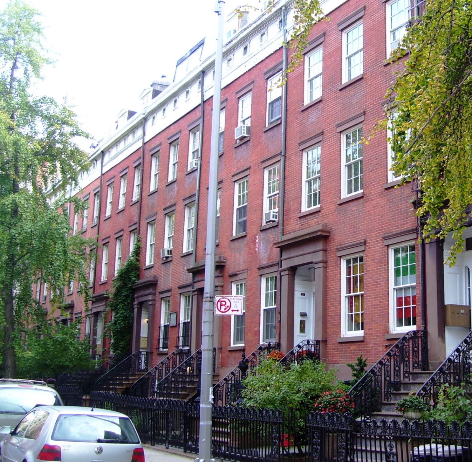 Cushman Row on West 20th Street, a line of red-brick Greek Revival rowhouses from the 1840s with iron railings, brownstone stoops, and consistent cornice lines along the tree-lined block