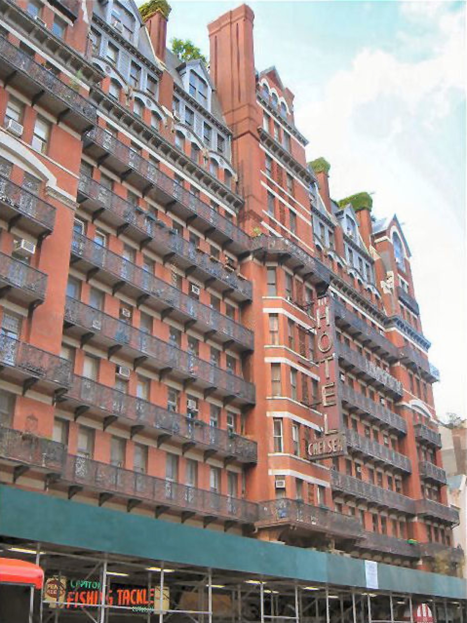 The Chelsea Hotel at 222 West 23rd Street, a twelve-story red-brick building with ornate wrought-iron balconies rising up its facade and the vertical HOTEL CHELSEA sign visible on the upper floors
