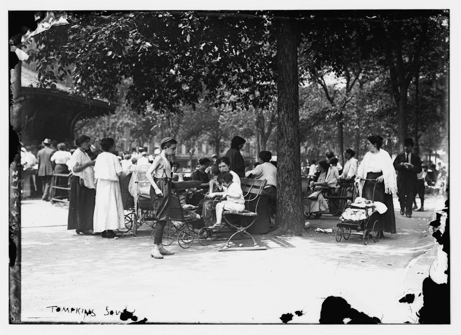 A tree-shaded gathering spot in Tompkins Square Park with benches beneath the mature elm canopy in the early 1900s