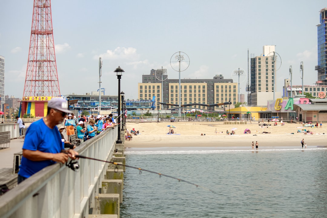 A person fishing on a pier next to a beach, representing the waterfront fishing culture that defines life along the southern shore of Gerritsen Beach