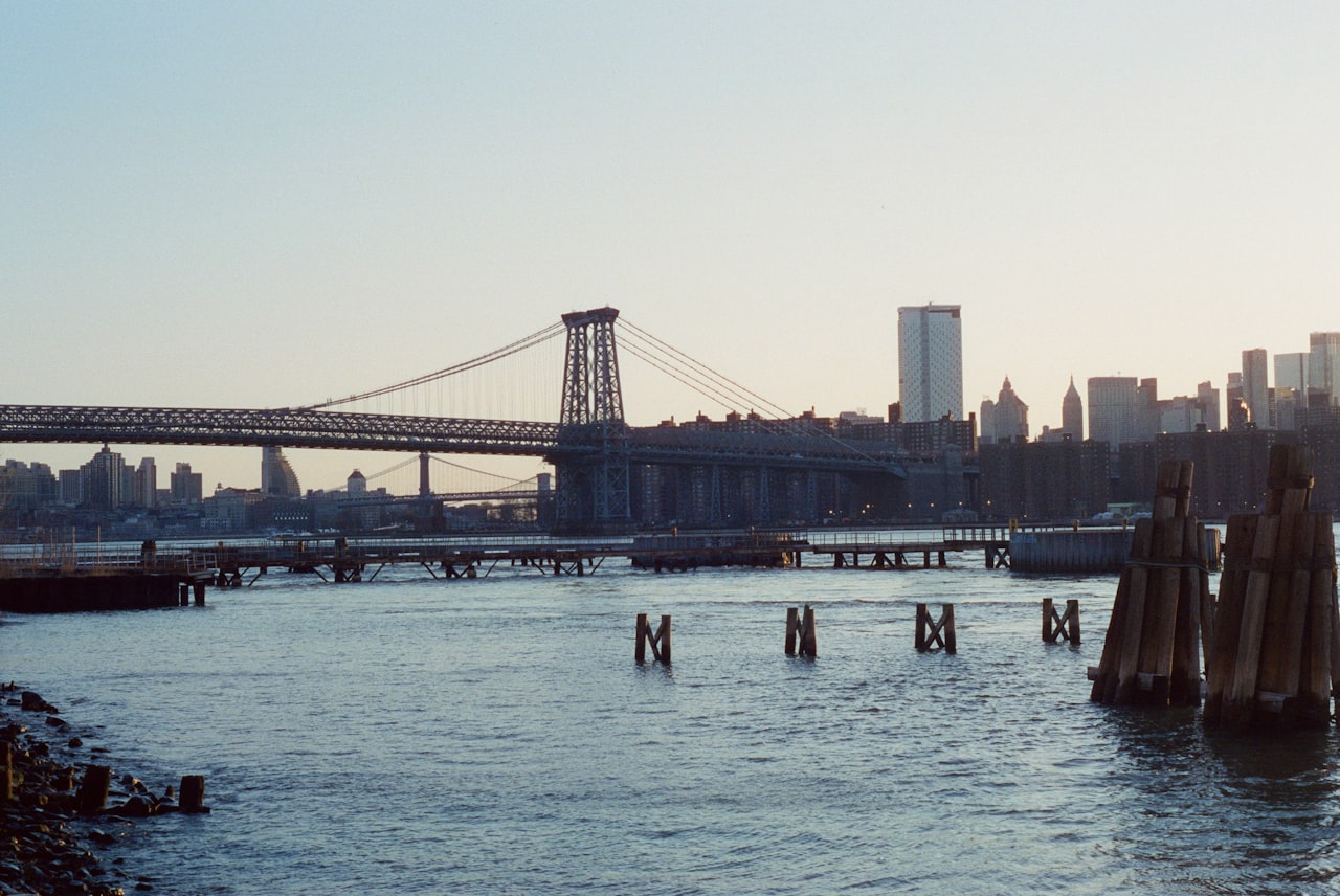 A view south along the Gowanus Canal in Brooklyn showing the dark water flanked by industrial brick buildings and a new residential tower under construction, with the Gowanus Expressway visible in the background against a clear sky