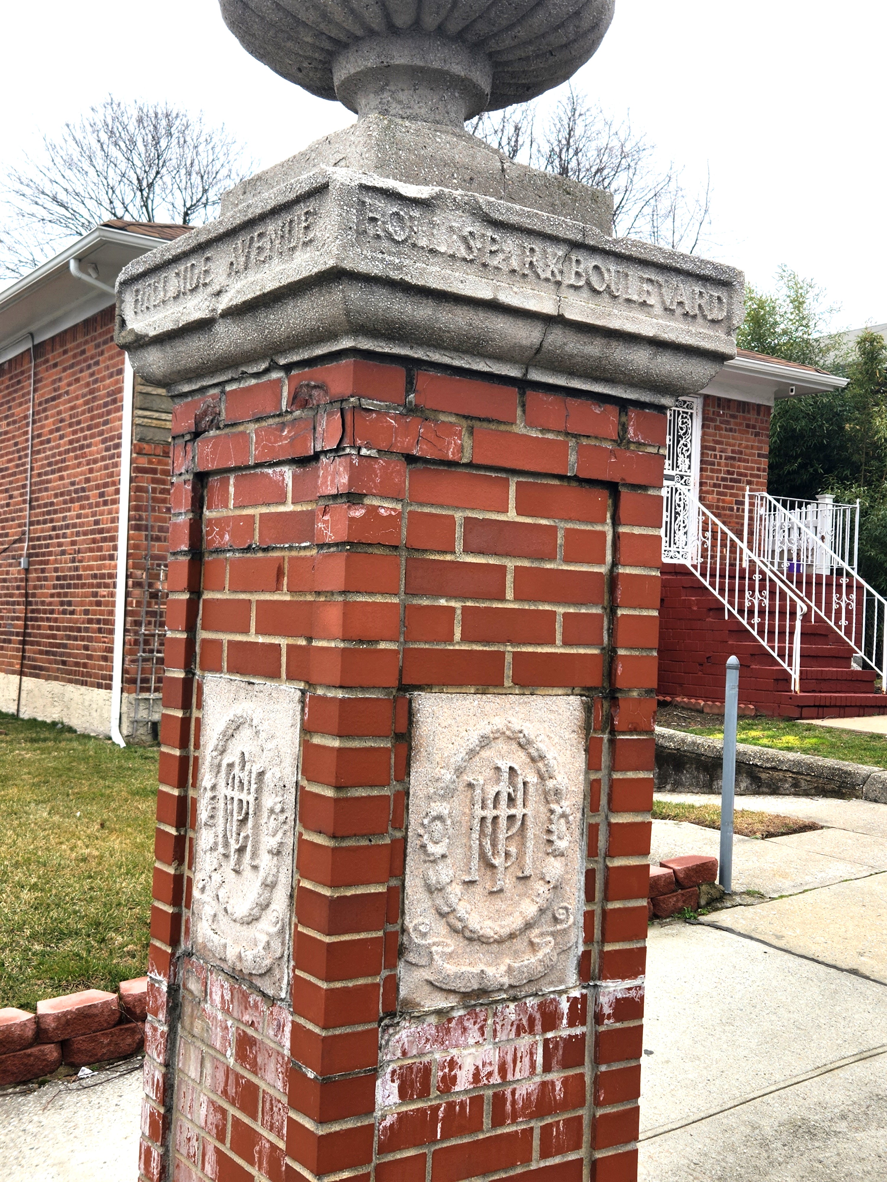 The corner marker at Hollis Park Boulevard, a Holliswood civic landmark set in brick and stone at the edge of the neighborhood's residential interior