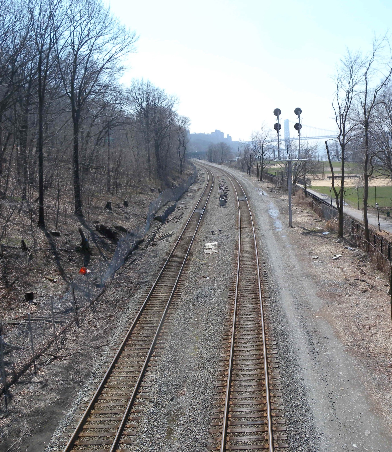 A wooded hillside inside Inwood Hill Park bordering the Metro-North rail cut with the Henry Hudson Bridge visible in the distance