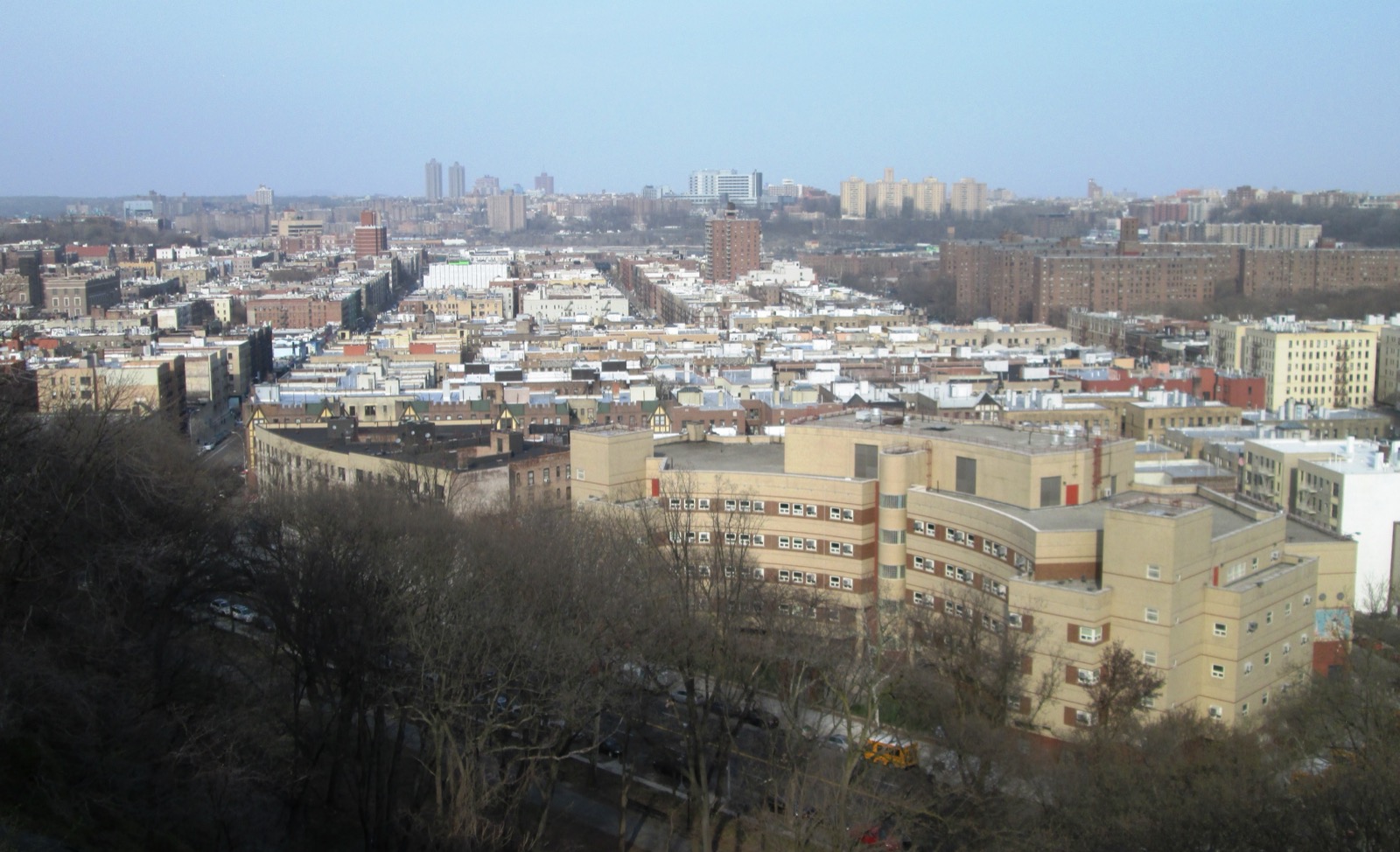 View of Inwood's pre-war apartment buildings and the Bronx skyline from Fort Tryon Park, showing the dense six-story brick walkup grid that defines the neighborhood