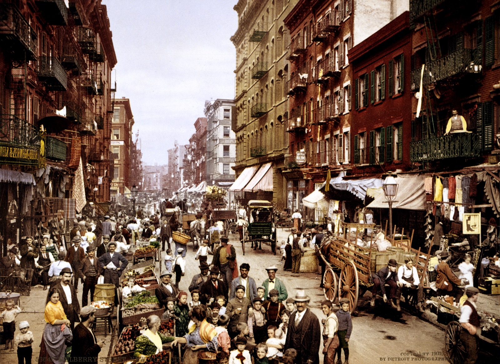Mulberry Street in Little Italy around 1900, crowded with pushcart vendors and lined with the tenement facades that still define the neighborhood today