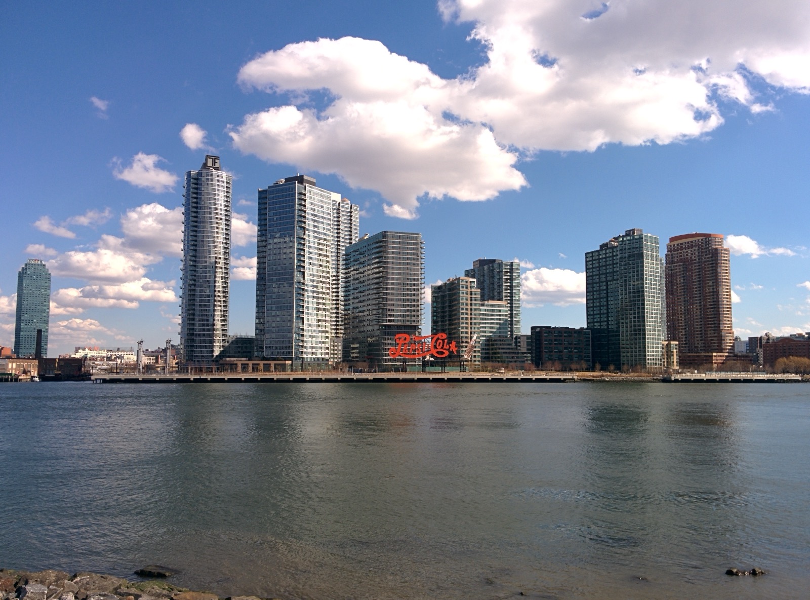 The Pepsi-Cola neon sign at Gantry Plaza State Park on the Long Island City waterfront with the East River and Manhattan skyline visible behind it