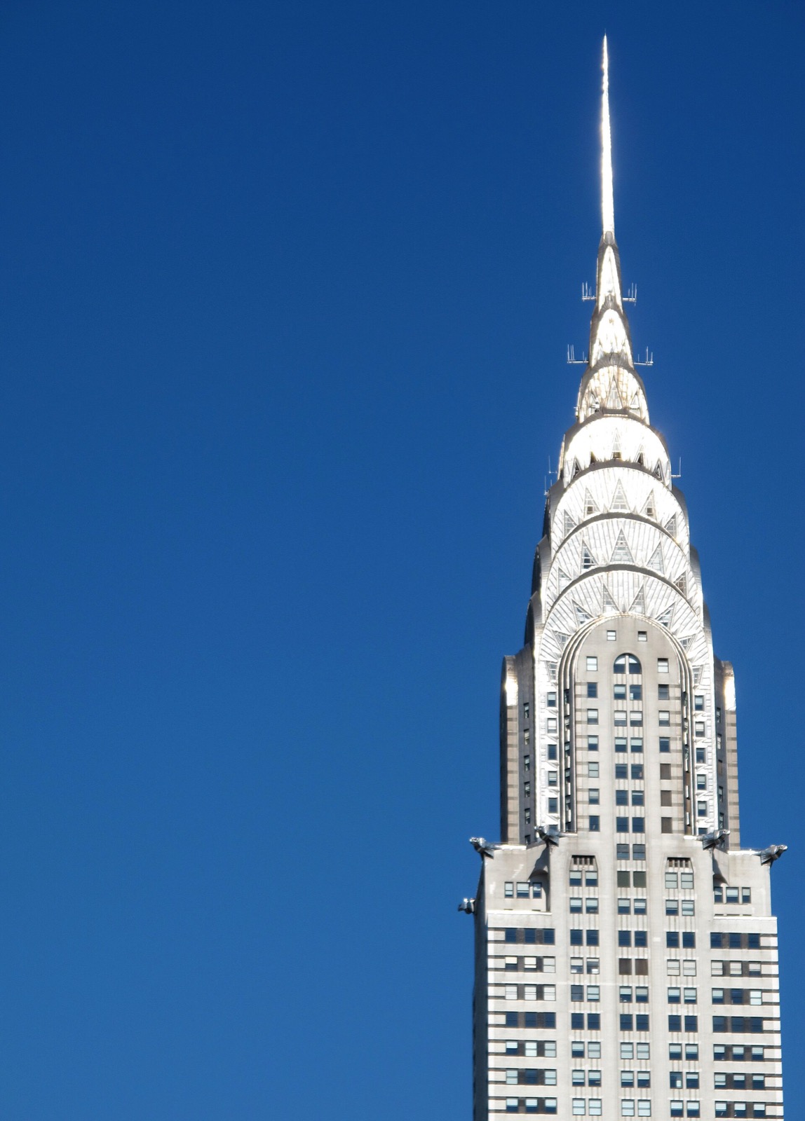 The Chrysler Building rising above Midtown Manhattan, its stainless steel Art Deco sunburst crown and eagle gargoyles visible against the sky