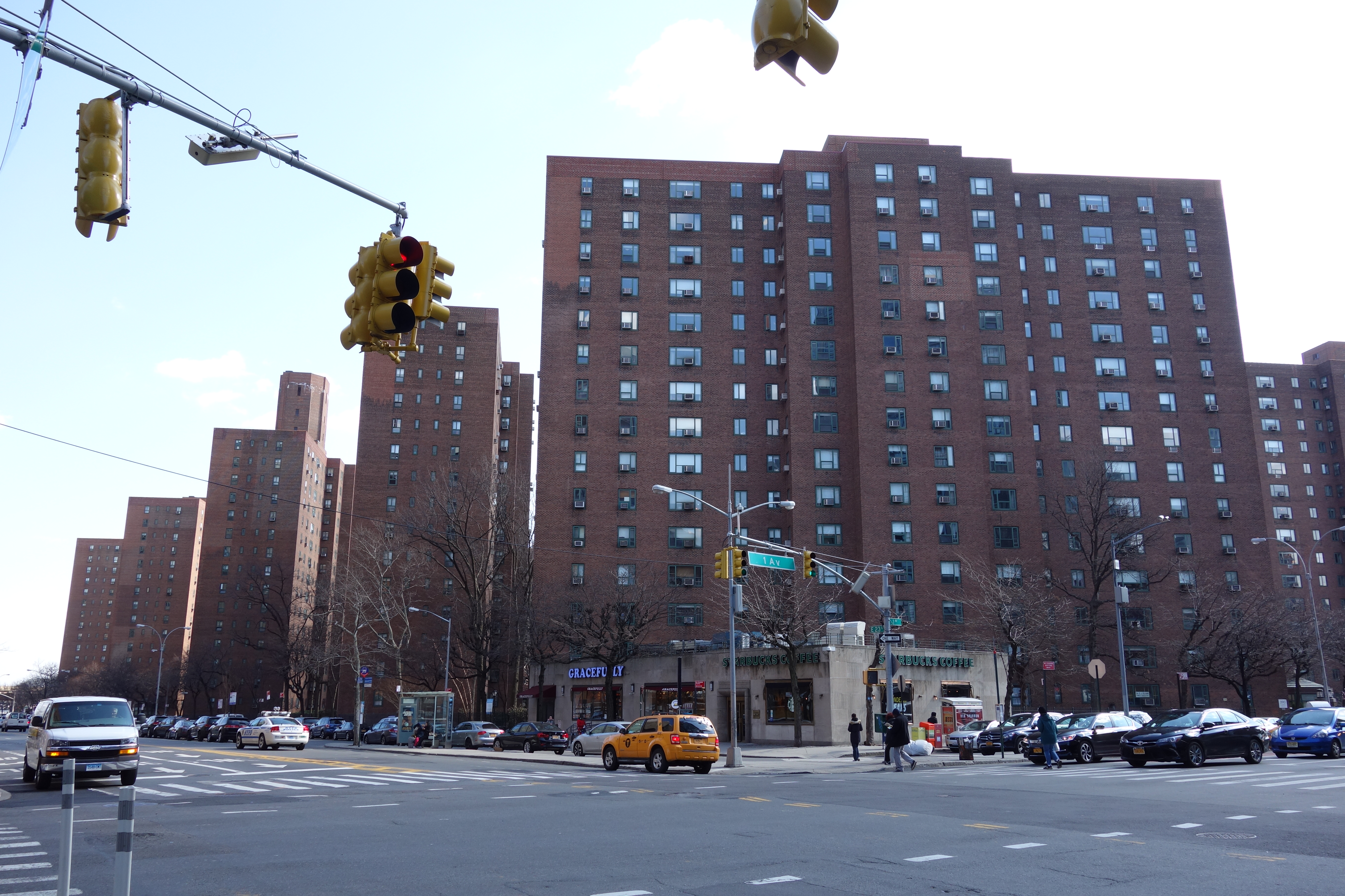 Red-brick mid-rise towers of Peter Cooper Village seen from East 23rd Street, showing the uniform 13-story buildings and the tree canopy of the complex beyond