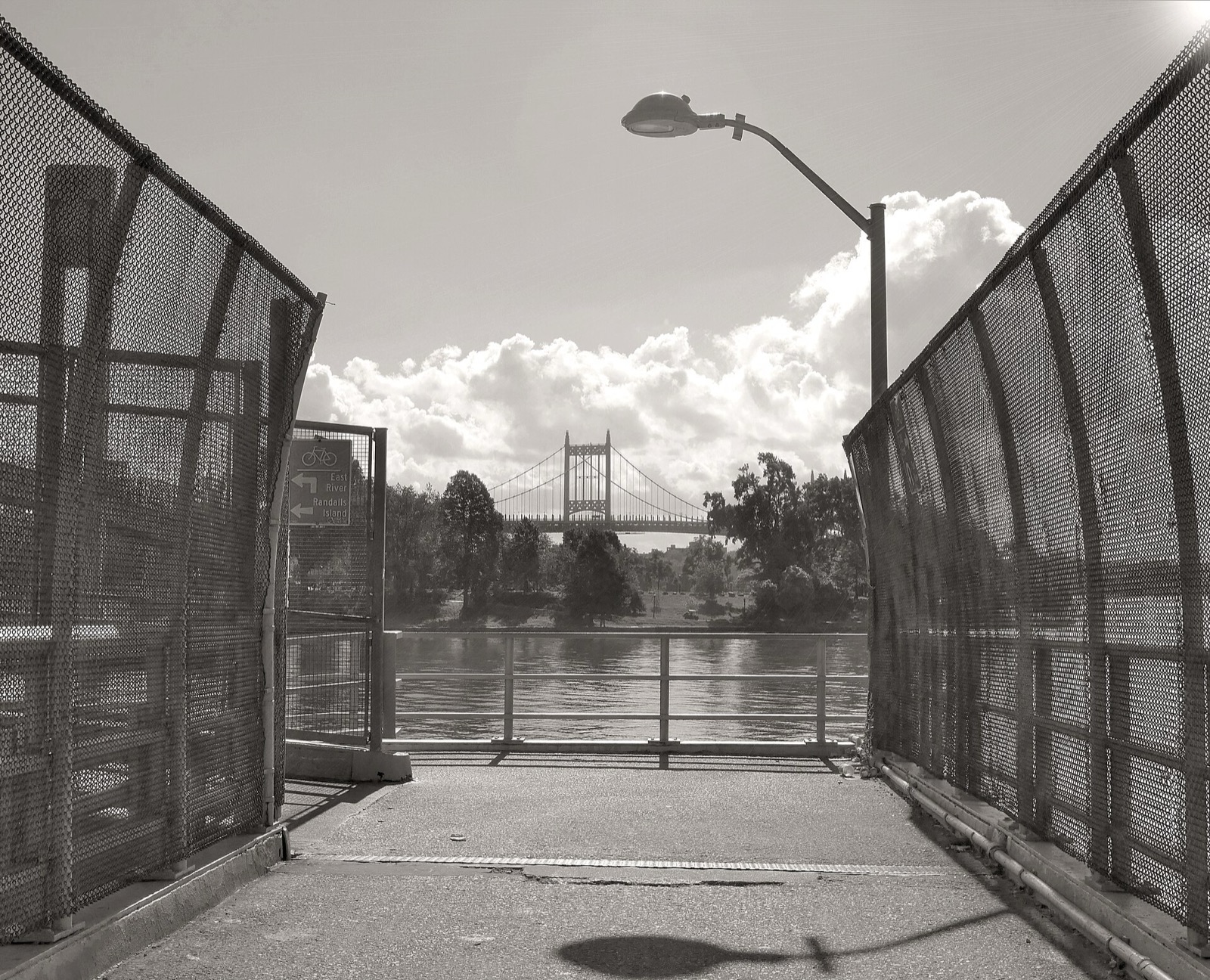 The 103rd Street pedestrian footbridge crossing from Manhattan to Randalls Island, with the Triborough Bridge visible in the background, the primary non-vehicular access point to the 480-acre island park