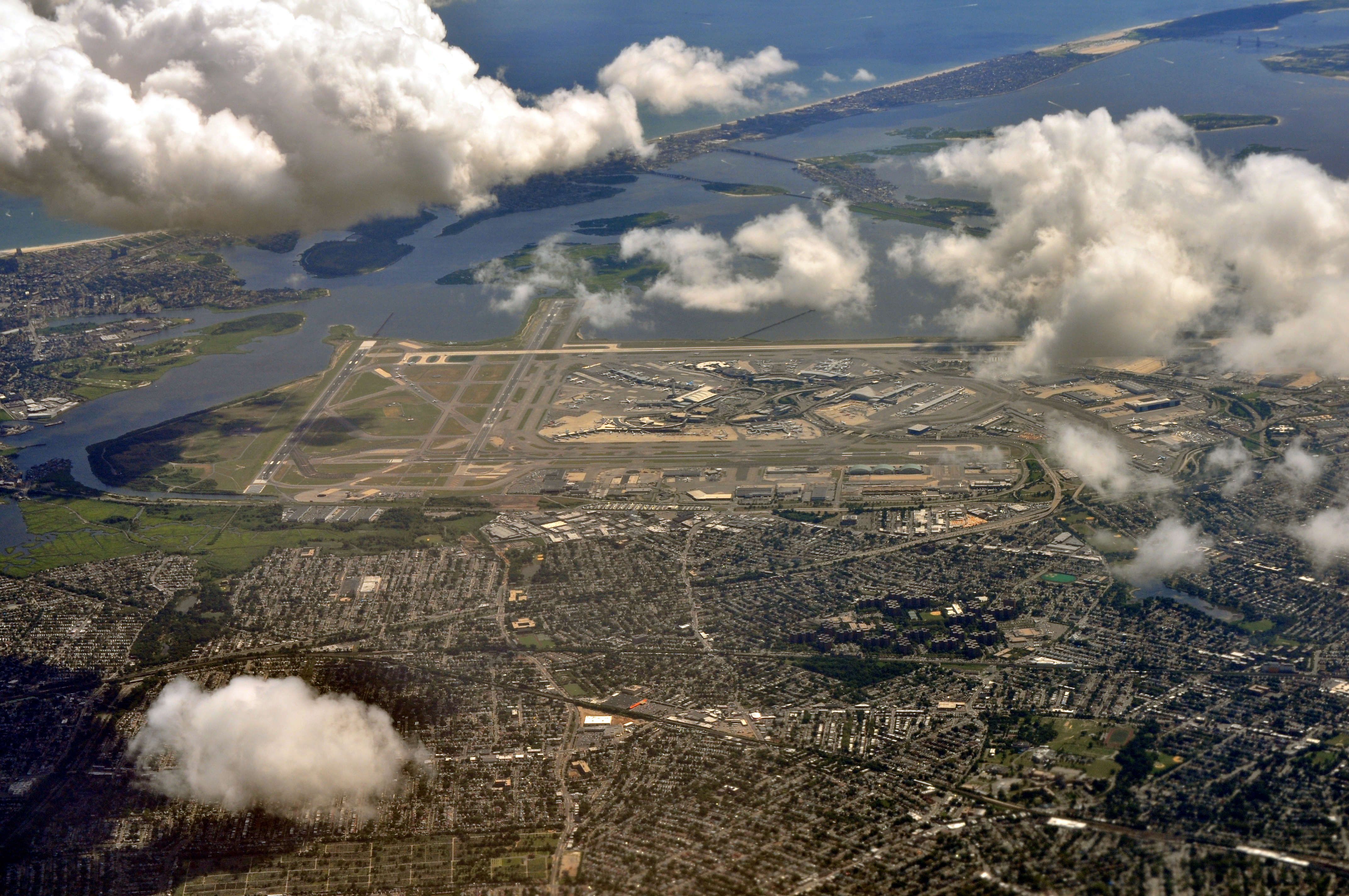 Aerial view of JFK International Airport looking northeast, showing the runways, terminals, and the surrounding southeast Queens residential neighborhoods including Springfield Gardens