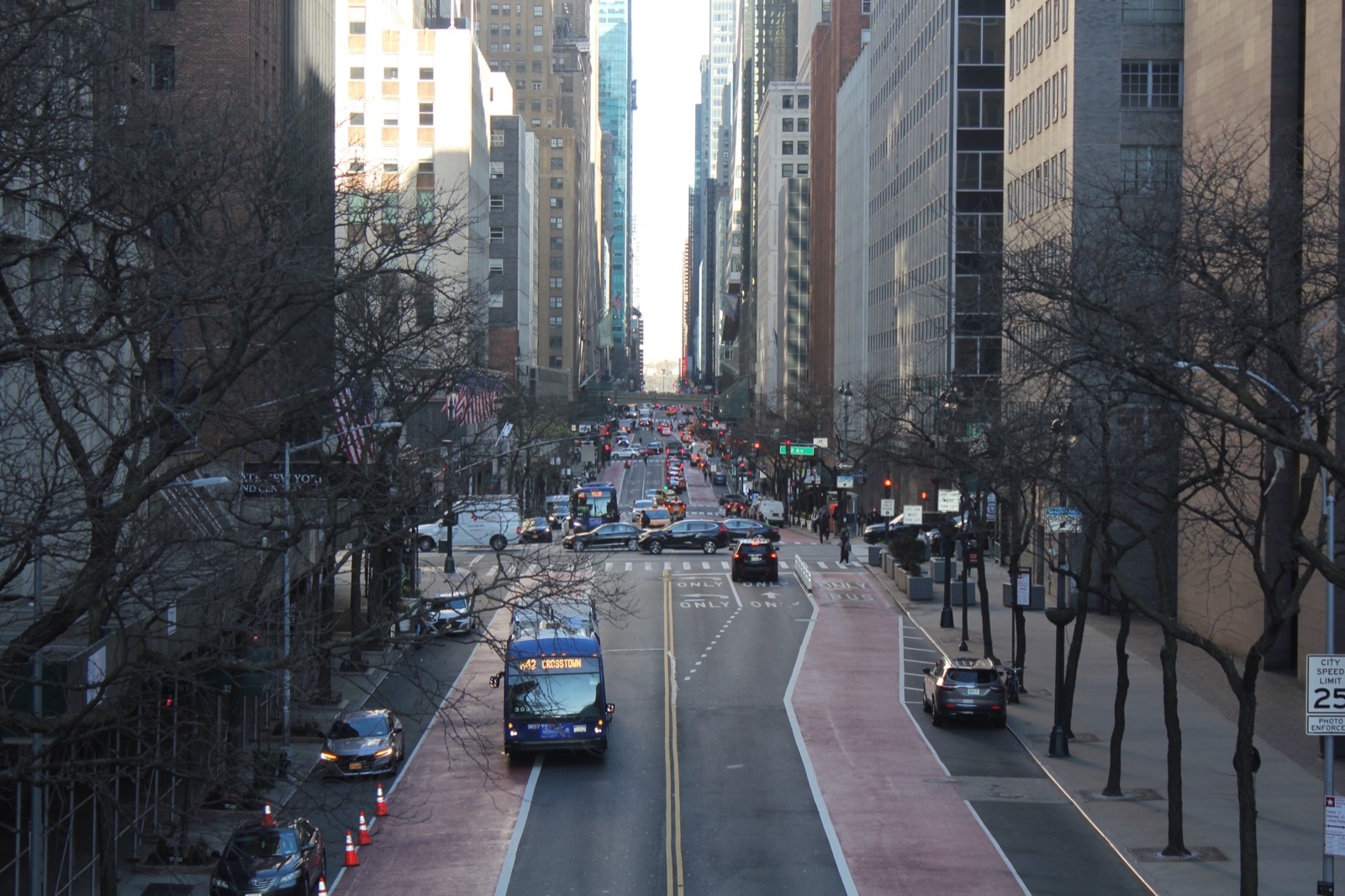 View of 42nd Street looking west from the Tudor City overpass, with Midtown Manhattan towers visible beyond and the elevated pedestrian bridge spanning the roadway below