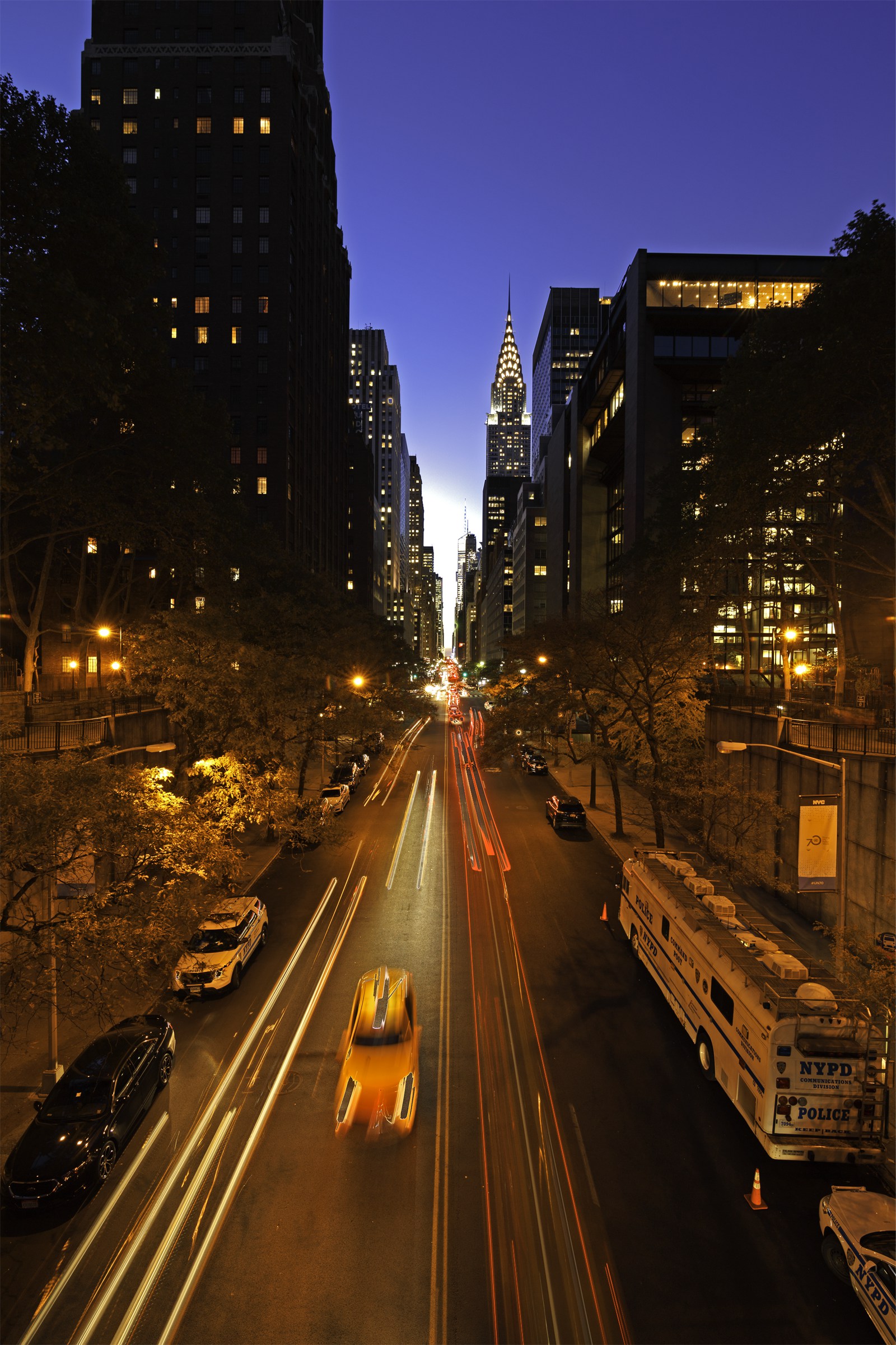 The Tudor City overpass at blue hour, looking west down 42nd Street with the Midtown Manhattan skyline visible through the Gothic arches of the pedestrian bridge