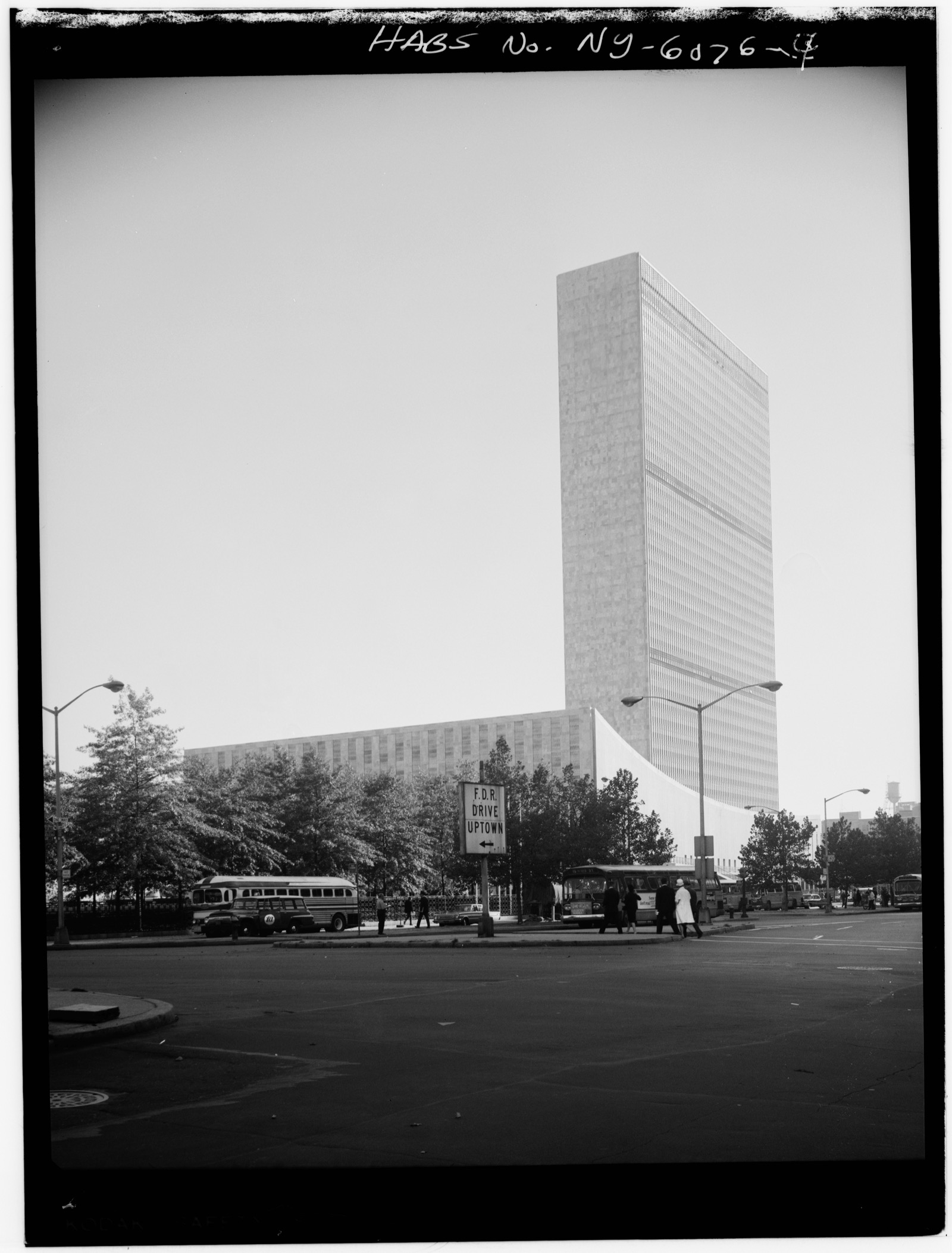 A black and white archival photograph of the United Nations Secretariat tower rising above the curved General Assembly Building in Turtle Bay