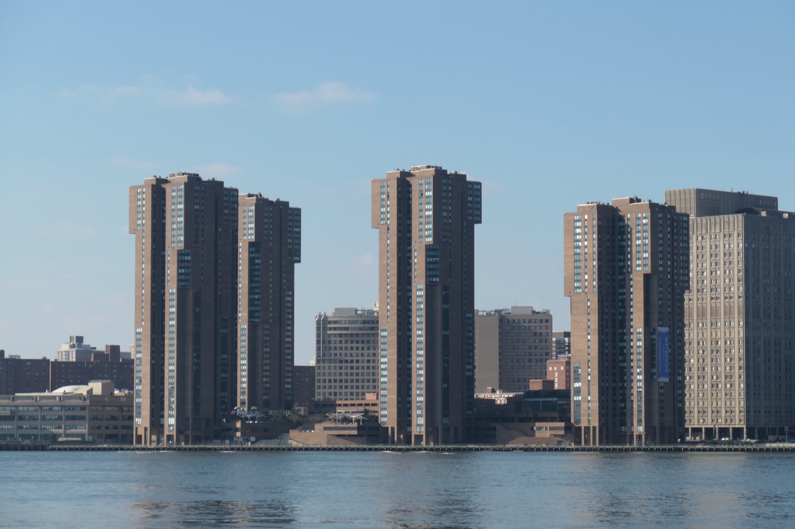 Waterside Plaza towers seen from across the East River, showing the residential complex rising directly from the water with the Manhattan skyline stretching behind it