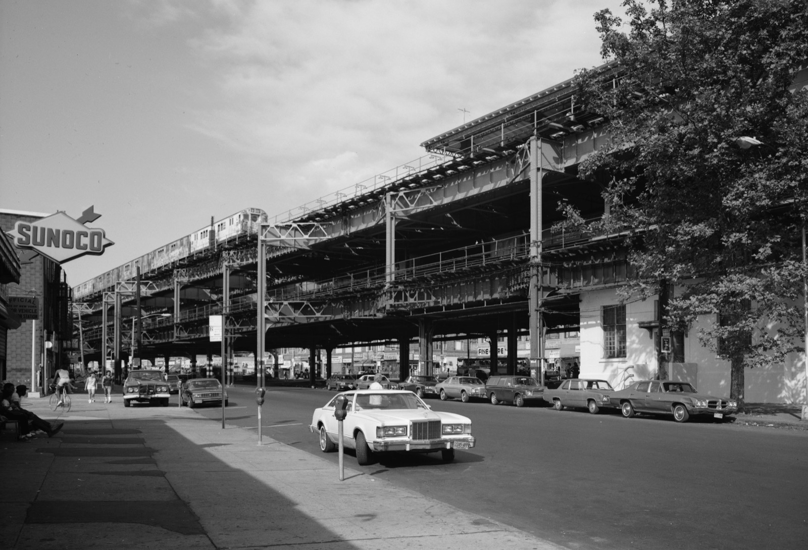 The IRT White Plains Road elevated subway line with its steel structure running above the commercial corridor, showing the distinctive pattern of light and shadow that defines the Williamsbridge streetscape