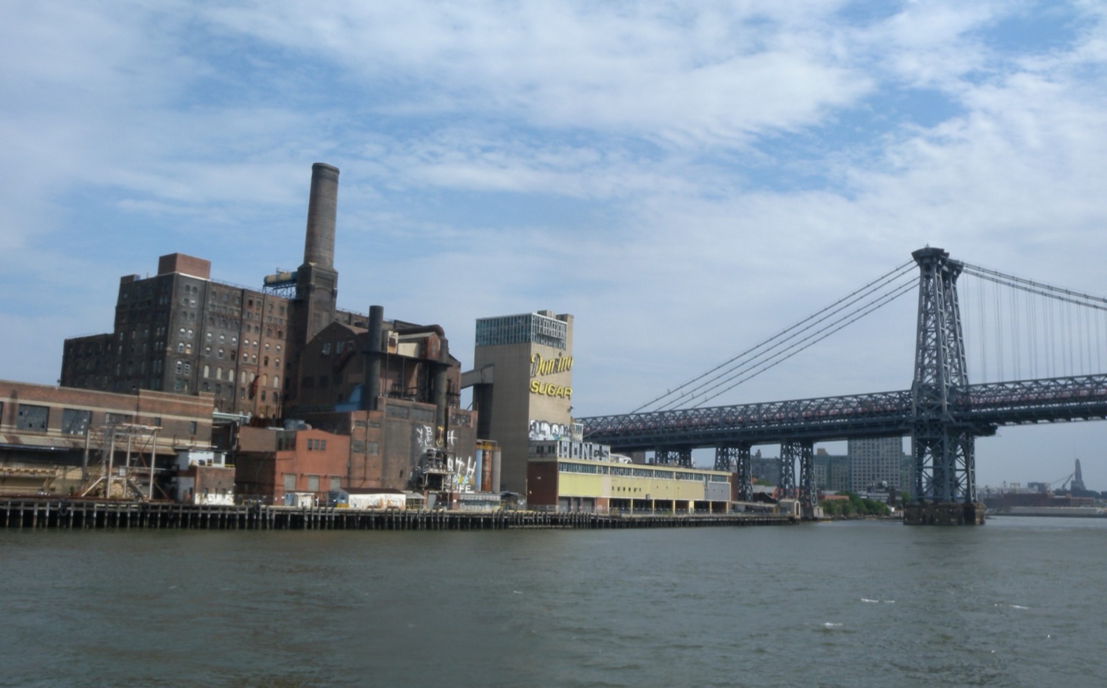 The former Domino Sugar Refinery building on the Williamsburg Brooklyn waterfront with its brick smokestack and rooftop sign next to the Williamsburg Bridge